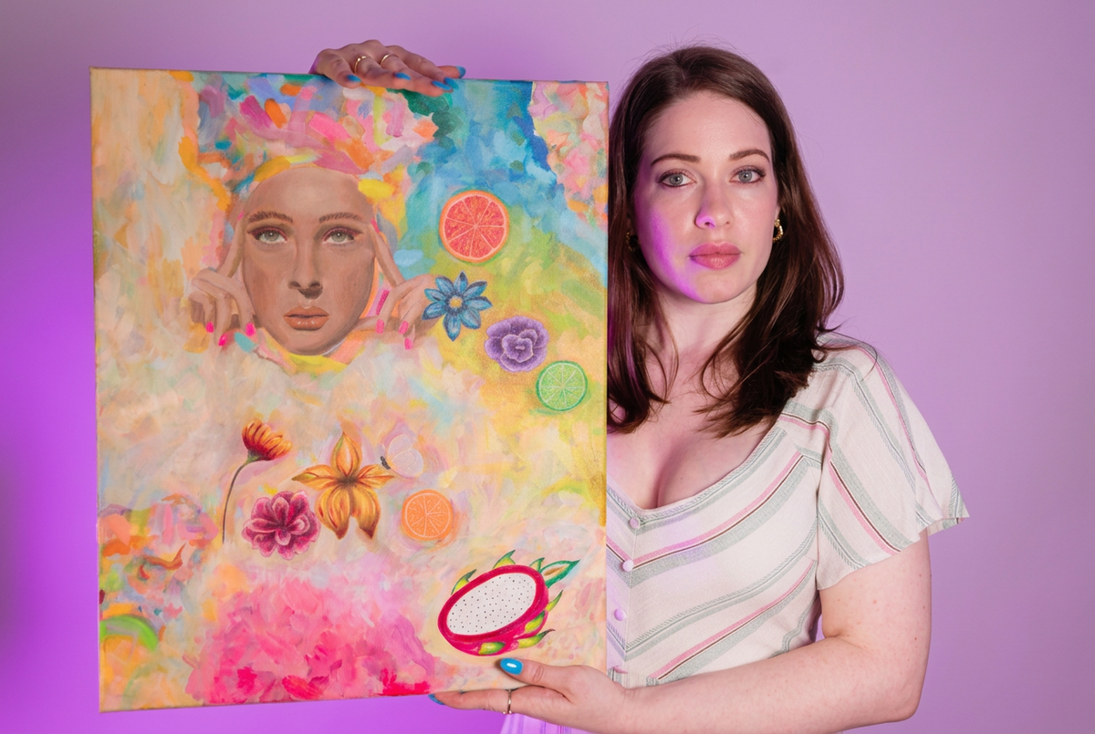 A picture of the Artist Kelly Schnobb holding up her painting “breakfast in Ibiza”