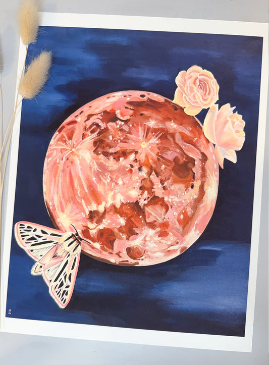 A rose quartz print with a design resembling a rose quartz crystall moon accompanied by floral elements and a moth, against a dark blue background.