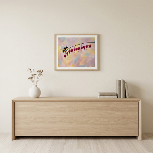 Hearts Nectar Print showing a bee and red heart-shaped flowers on a pastel background, in a light wood frame above an oak console.