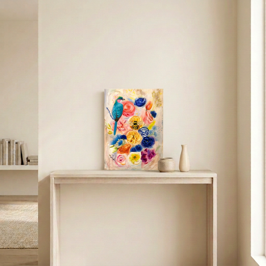 July's Bouquet original painting, a 12 x 16 inch canvas of vibrant summer flowers with a turquoise bird and bumblebee, hanging unframed above a pale wood console in a warm neutral room