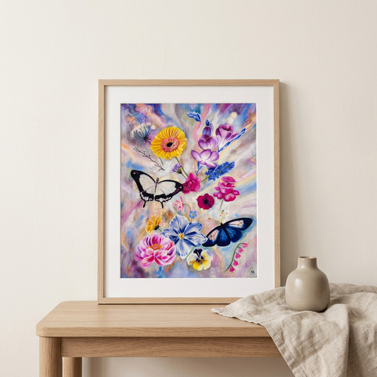 Sunstone floral and butterfly print styled in an oak frame on a light wood console against an ivory wall.